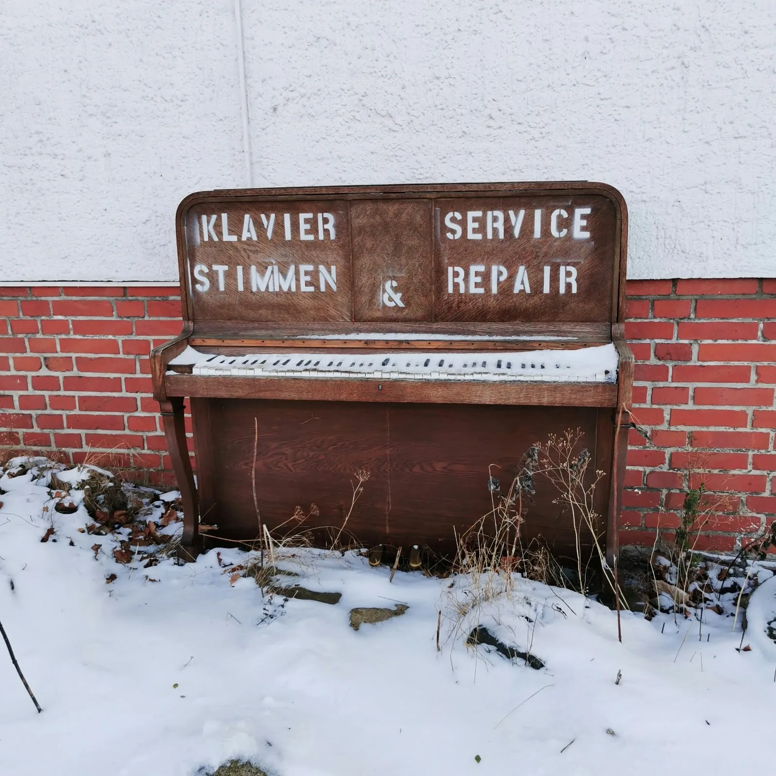 Altes Klavier im Schnee vor einer Ziegelwand mit Werbeaufschrift